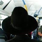 man standing on bus with large black hat