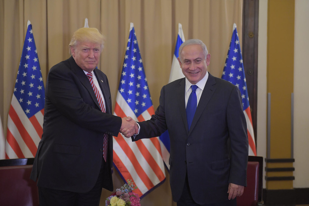 Trump and Netanyahu shaking hands in front of American and Israeli flags