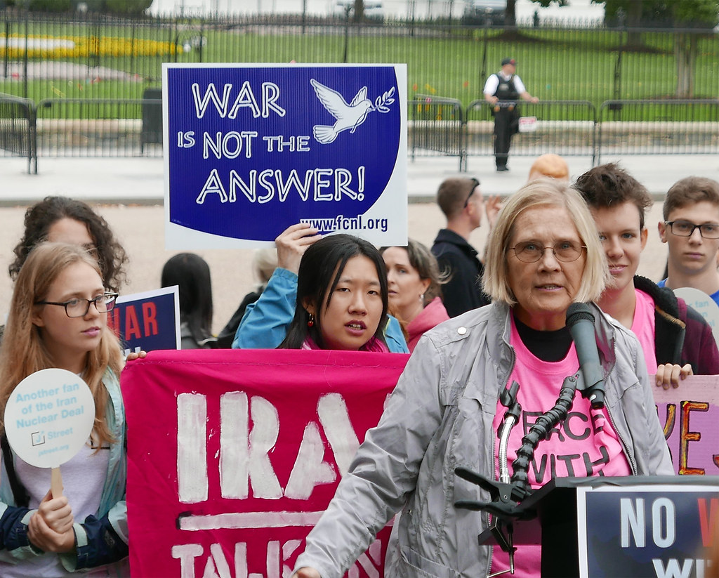 Image of a protest against war with Iran. Woman speaking at podium