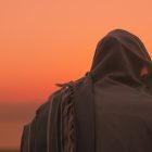 A husband and wife huddle together under the husband's prayer shawl after his sunrise prayer at Masada, Israel.